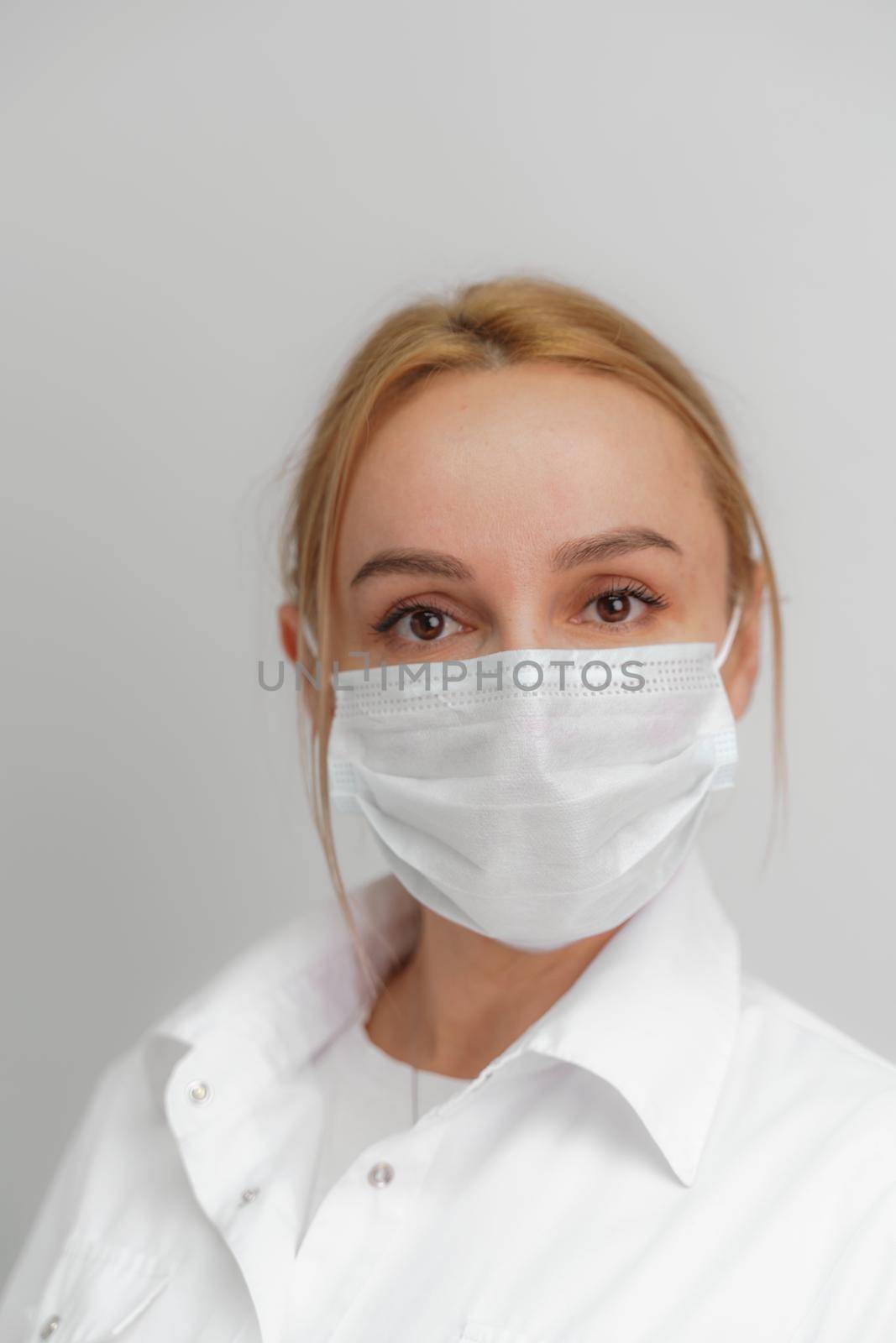 Close-up portrait of a young blonde woman in a medical mask on a light background. Virus protection. Coronovirus covid-19 The concept of a pandemic epidemic. Quarantine. Stay at home. by Matiunina