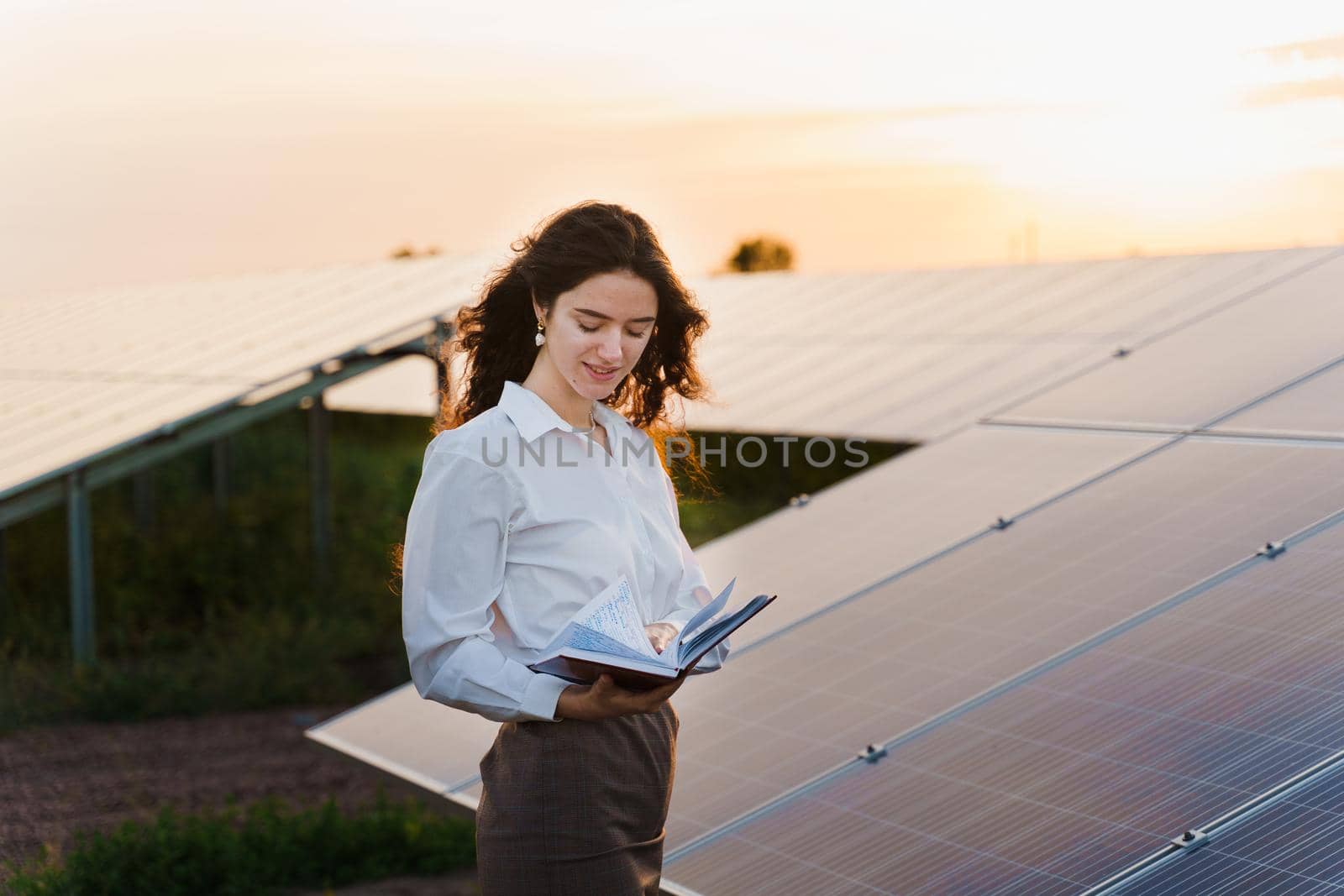 Girl and solar panels stands in row on the ground at sunset. Solar cells power plant business. by Rabizo