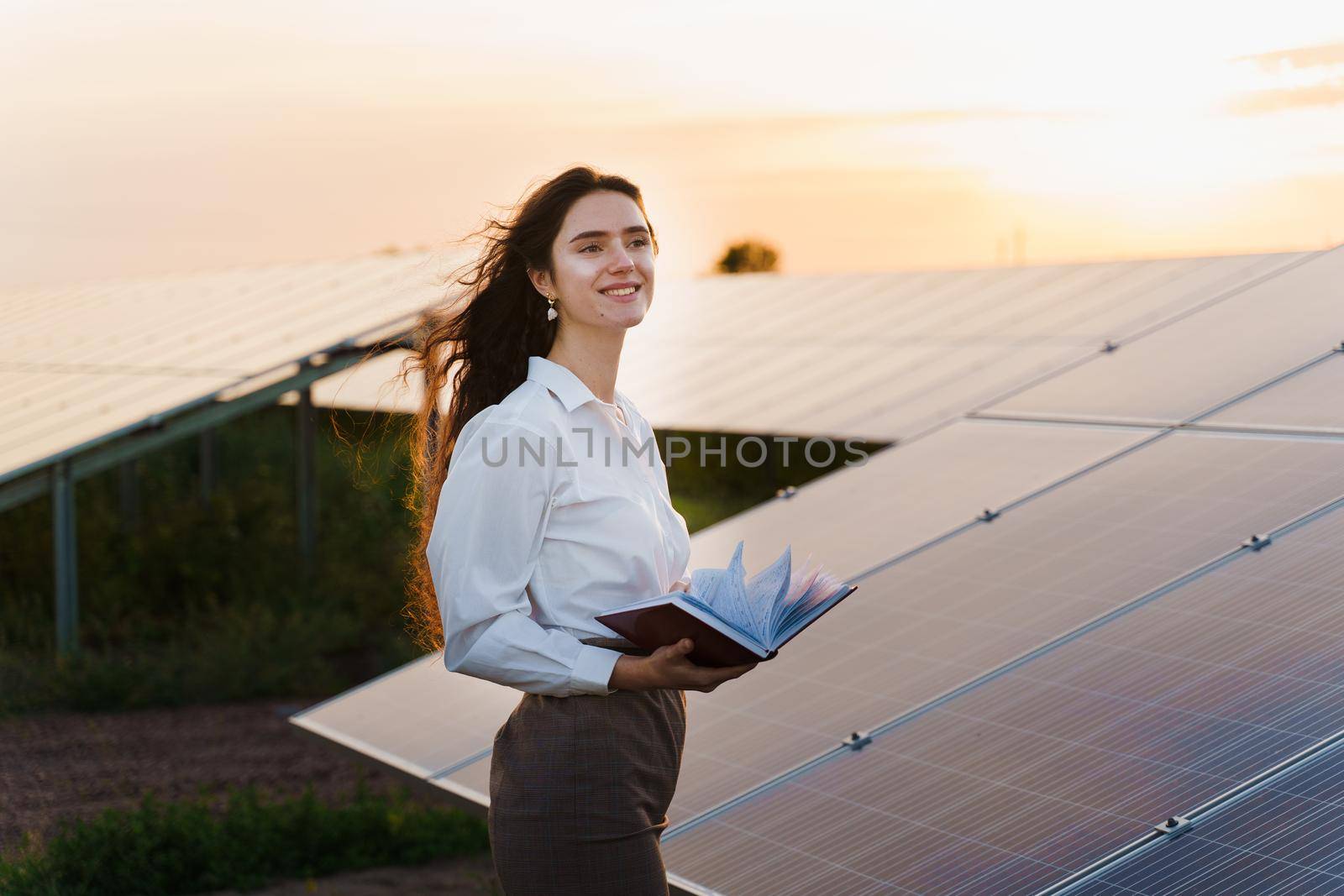 Girl and solar panels stands in row on the ground at sunset. Solar cells power plant business