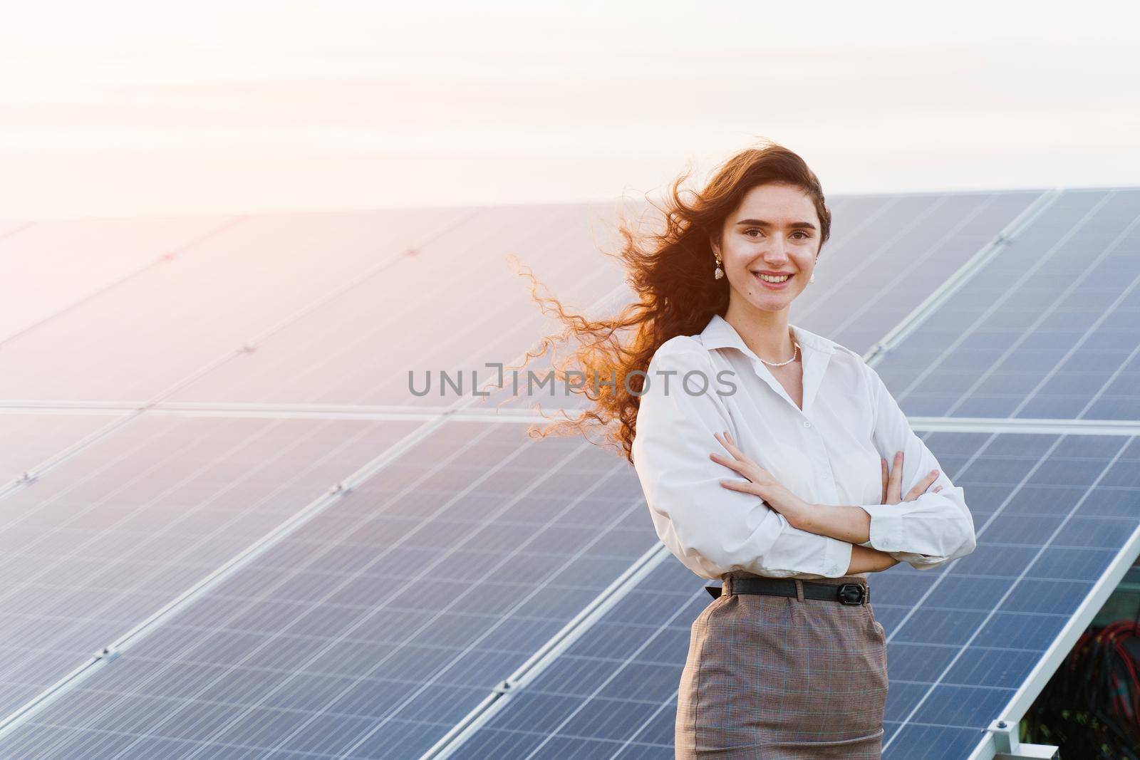 Model with solar panels stands in row on the ground. Girl dressed white formal shirt smiles on the power plant. by Rabizo