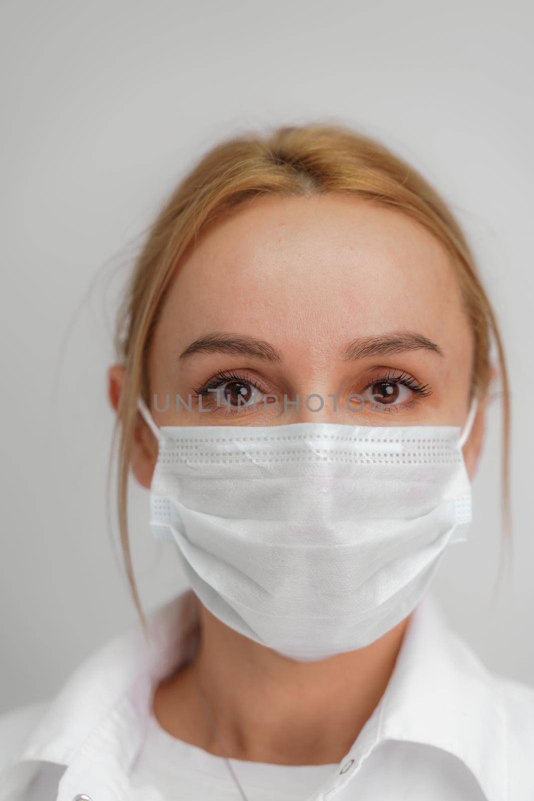 Close-up portrait of a young blonde woman in a medical mask on a light background. Virus protection. Coronovirus covid-19 The concept of a pandemic epidemic. Quarantine. Stay at home. by Matiunina