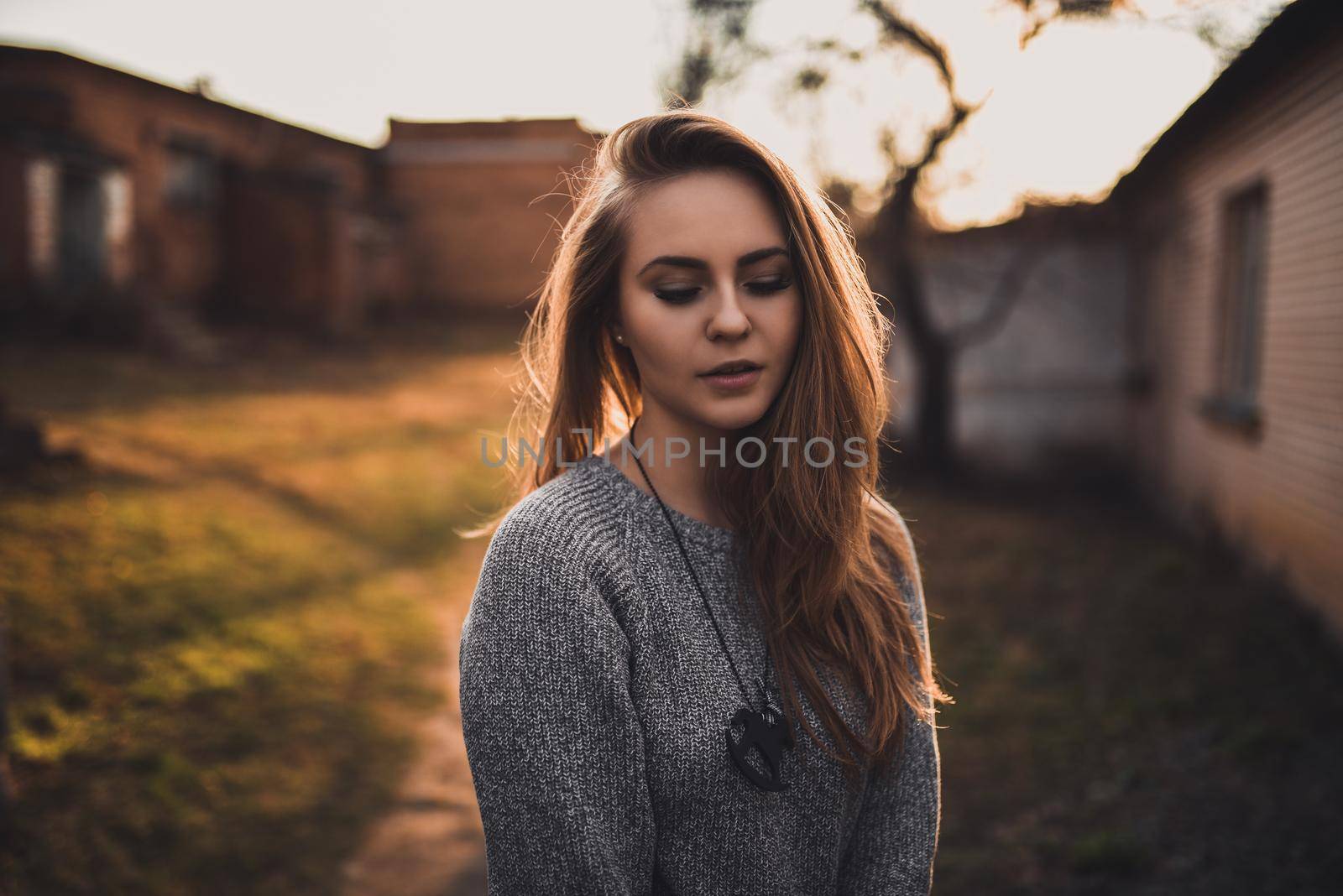 beautiful young blonde model girl. gray knitted sweater. wooden pendant on the neck in the form of a horse. On the Sunset. Portrait. best retouch