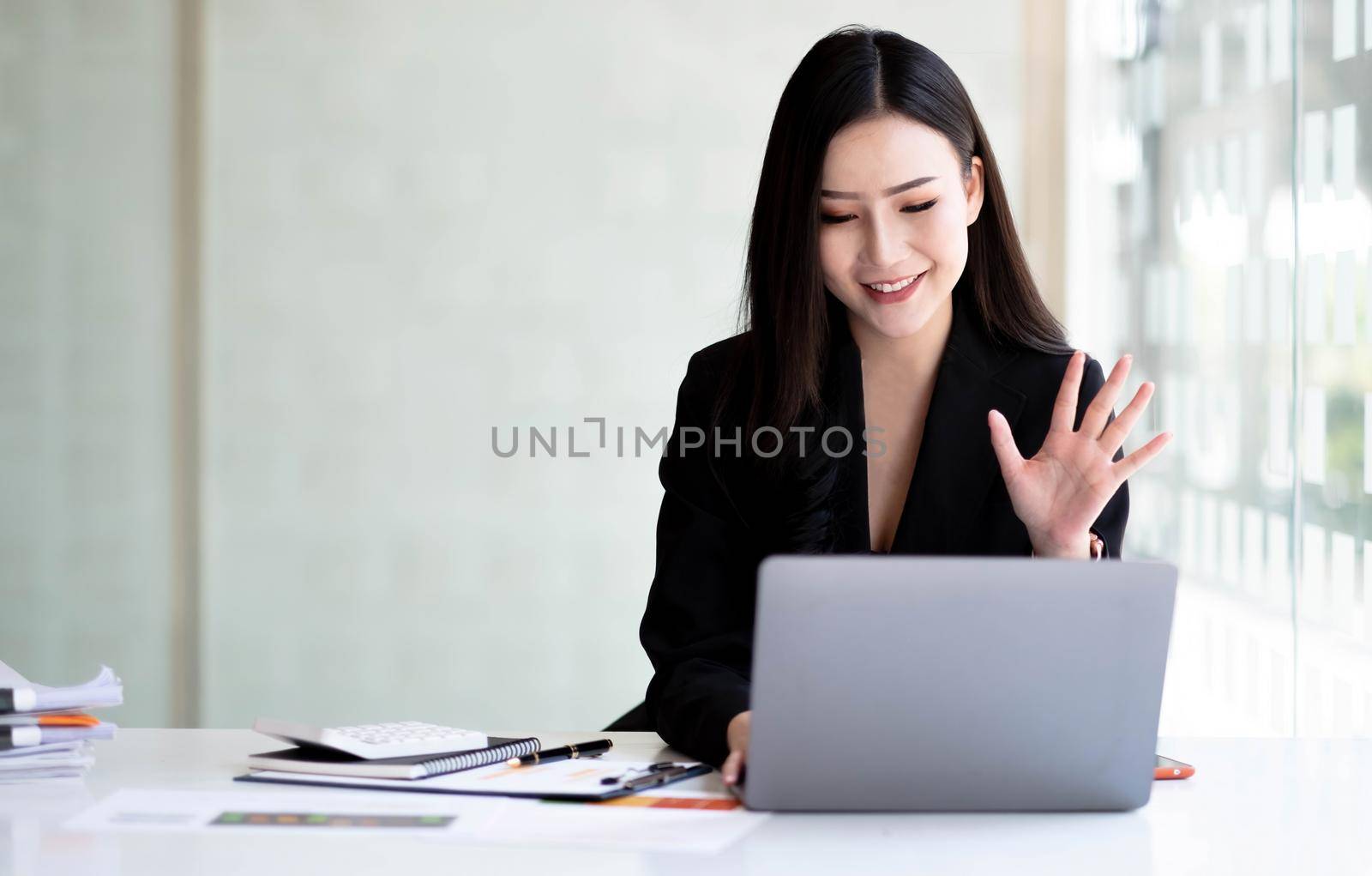 Shot of Asian young business woman looking and speaking through the webcam while making a video conference from the office. by wichayada