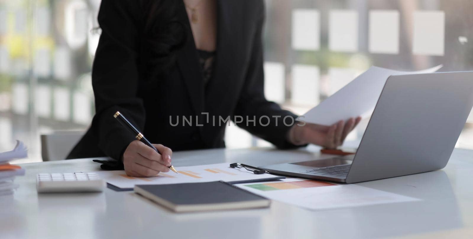Businesswoman holding pen and pointing paper chart summary analyzing annual business report with using laptop at room office desk..