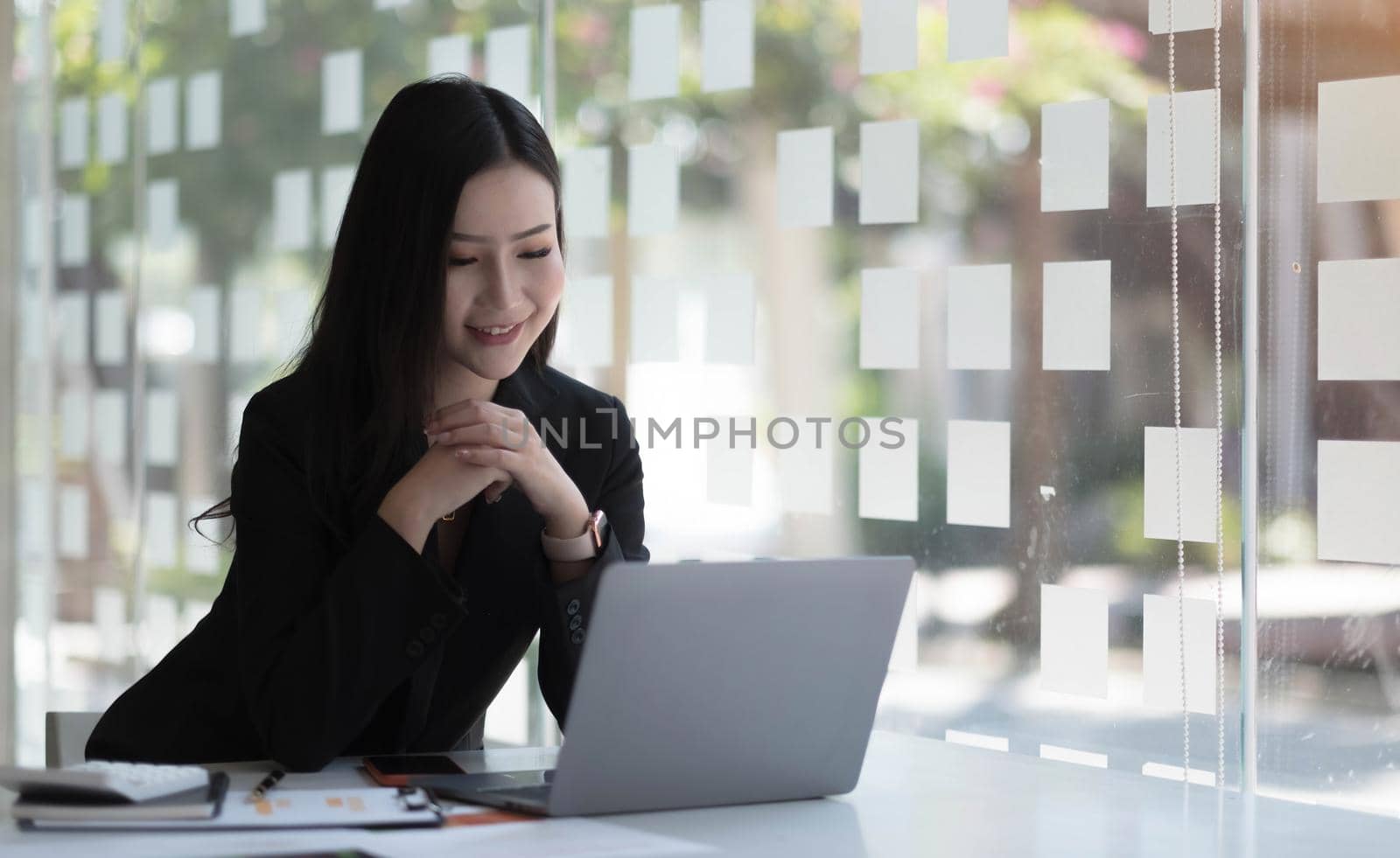 Charming asian businesswoman sitting working on laptop in office. by wichayada