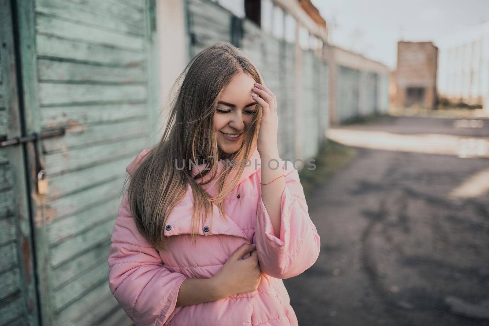 Young gorgeous blonde girl dressed fashion pink jacket and blue jeans. Old azure cerulean fence on the background. Picture ideal for illustrating women's magazines.