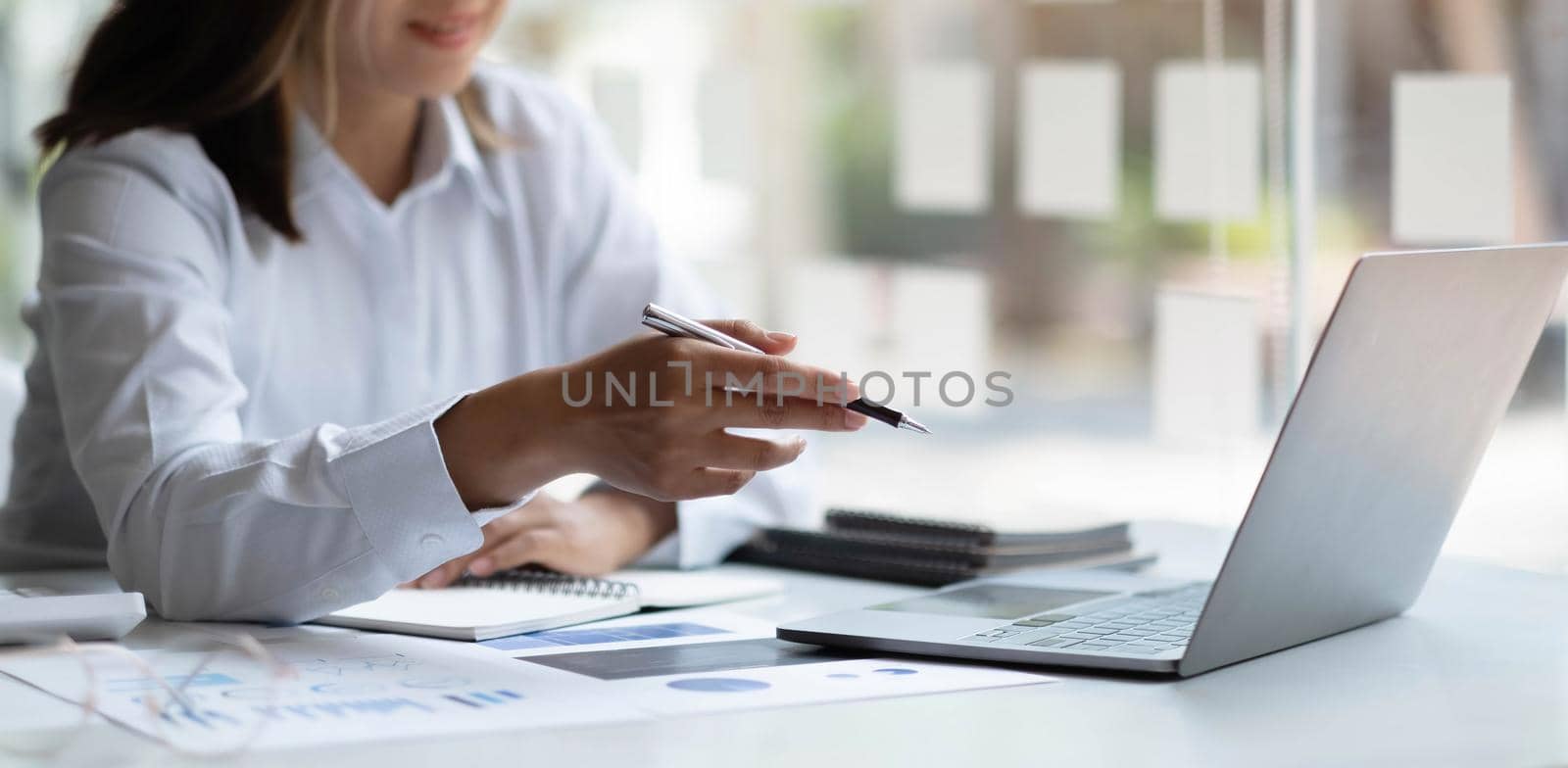 Beautiful smiling Asian businesswoman wearing glasses hand holding pen working using tablet at office.