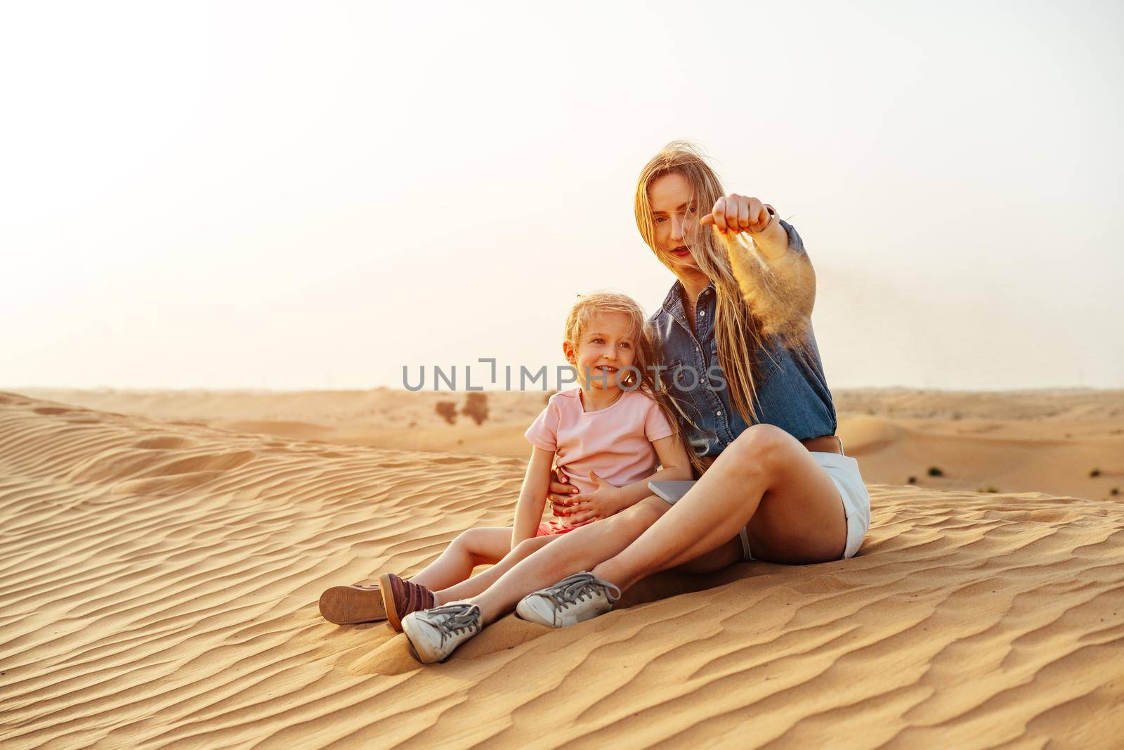 Mother and daughter sitting together on sand dune in the Dubai desert by Fabrikasimf