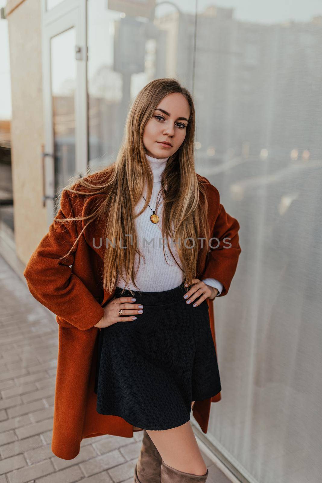 young blonde woman in autumn clothes walks on street background shop windows. Street style Fashion 2021 Winter Spring Terracotta Coat Woolen Cashmere Suede Over Knee Boots White Golf