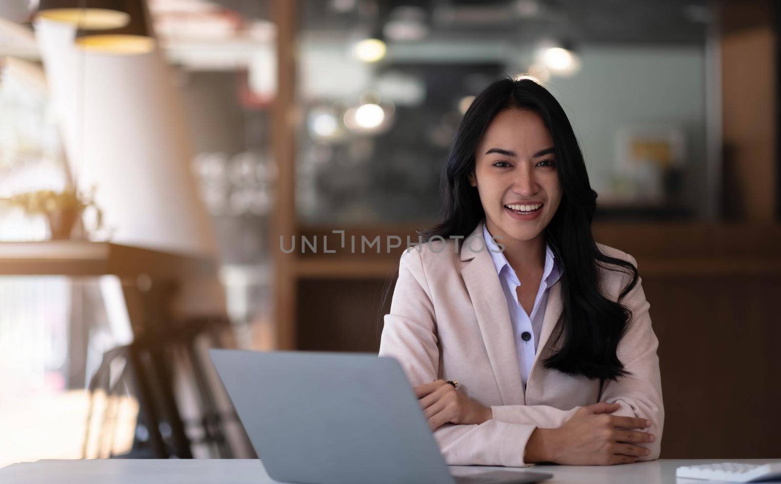 Charming Asian businesswoman working with a laptop at the office. Looking at camera..