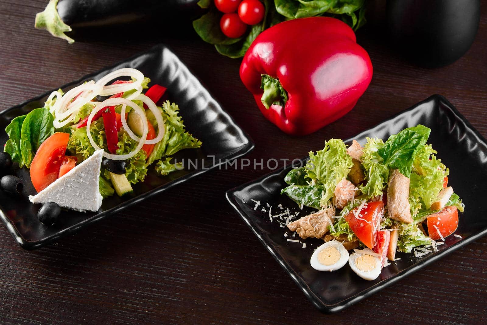 Greek salad, Caesar on black square plates on dark wooden table