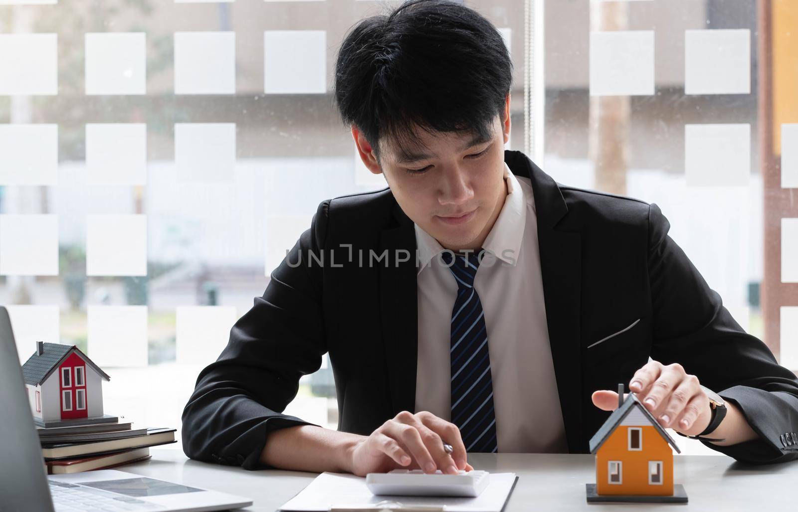 Real estate agent with model of house use calculator for sale,real estate agent home loan working at the office. by wichayada