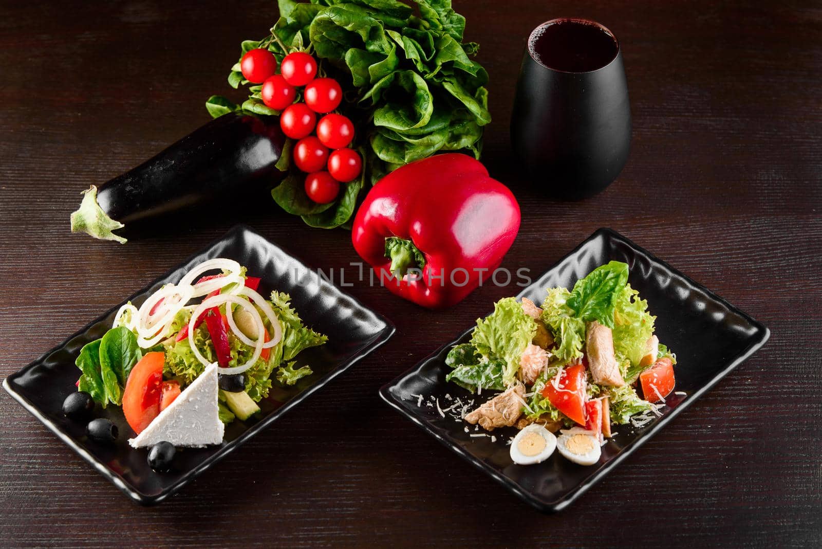 Greek salad, Caesar on black square plates on dark wooden table