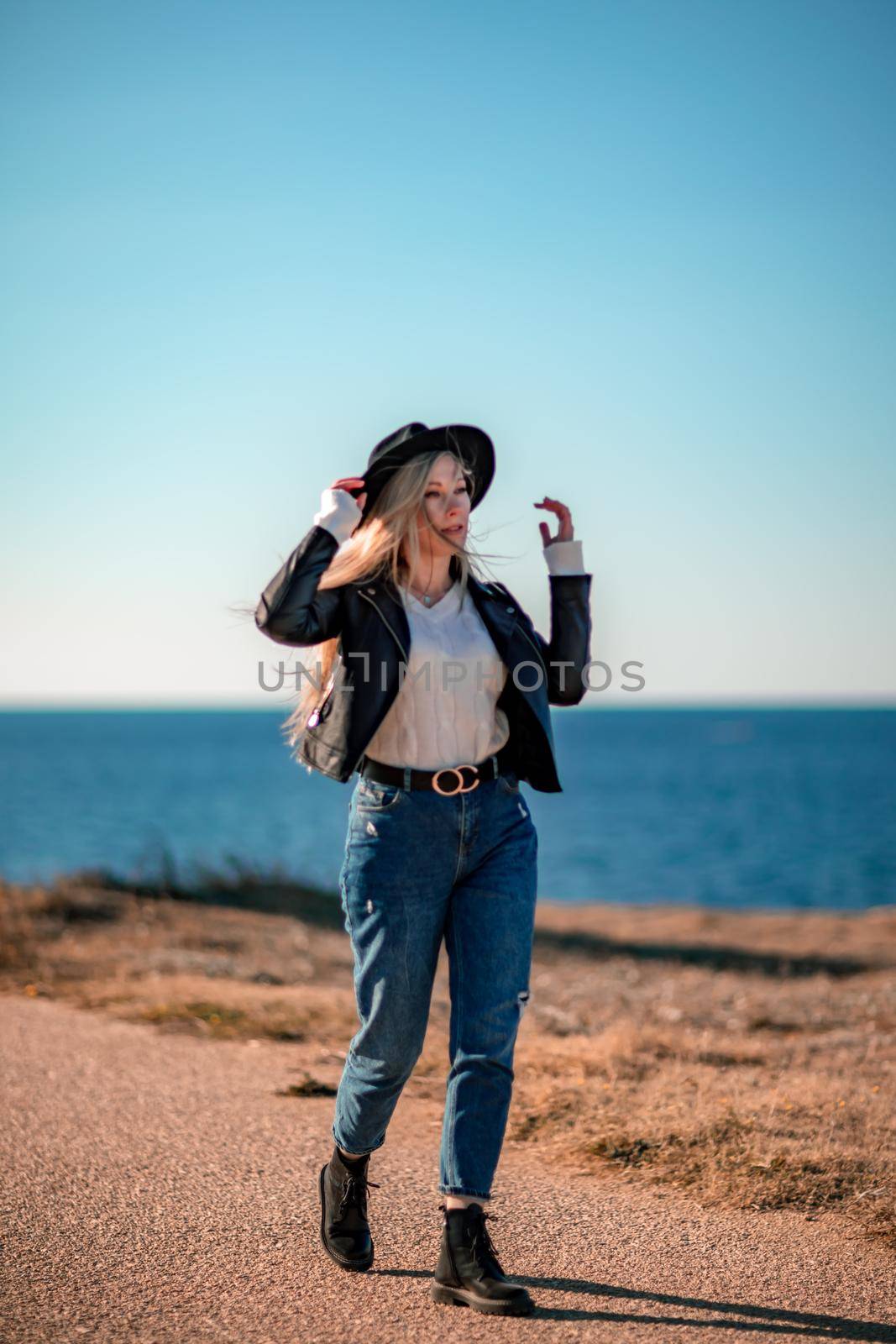 A blonde in a stylish black leather jacket walks along the seashore. by Matiunina