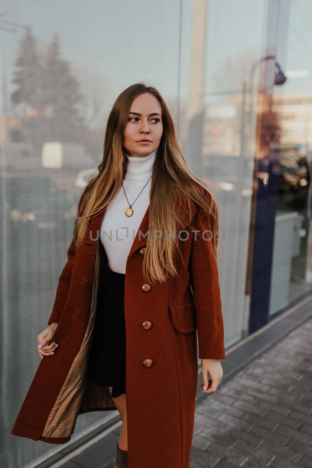 young blonde woman in autumn clothes walks on street background shop windows. Street style Fashion 2021 Winter Spring Terracotta Coat Woolen Cashmere Suede Over Knee Boots White Golf