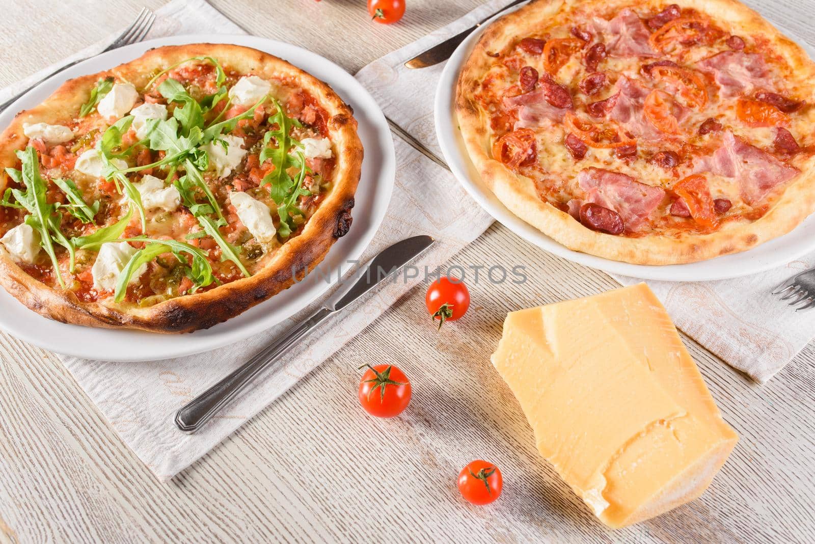 Pizza with salmon, feta cheese, sausages, ham, salami and sauce, tomatoes, on white round plate on light wooden table