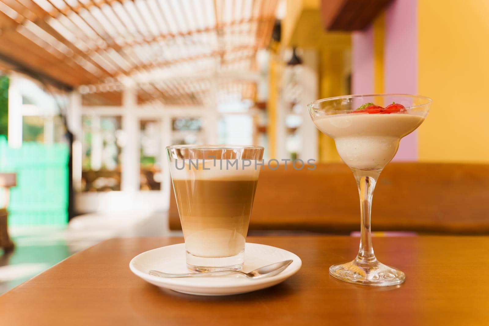 Creamy dessert with strawberries in glass, cappuccino on wooden table. Appetizing dessert and latte on the background of the restaurant.