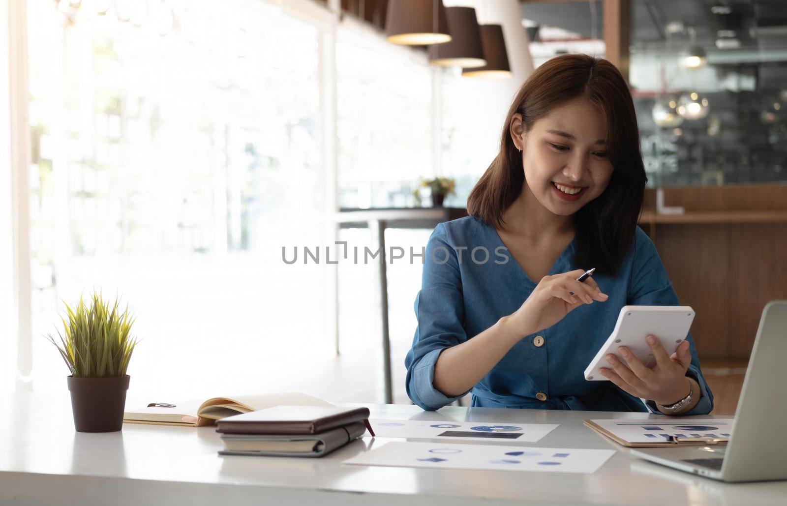 Business asian woman using calculator for do math finance on wooden desk in office, tax, accounting, financial concept.