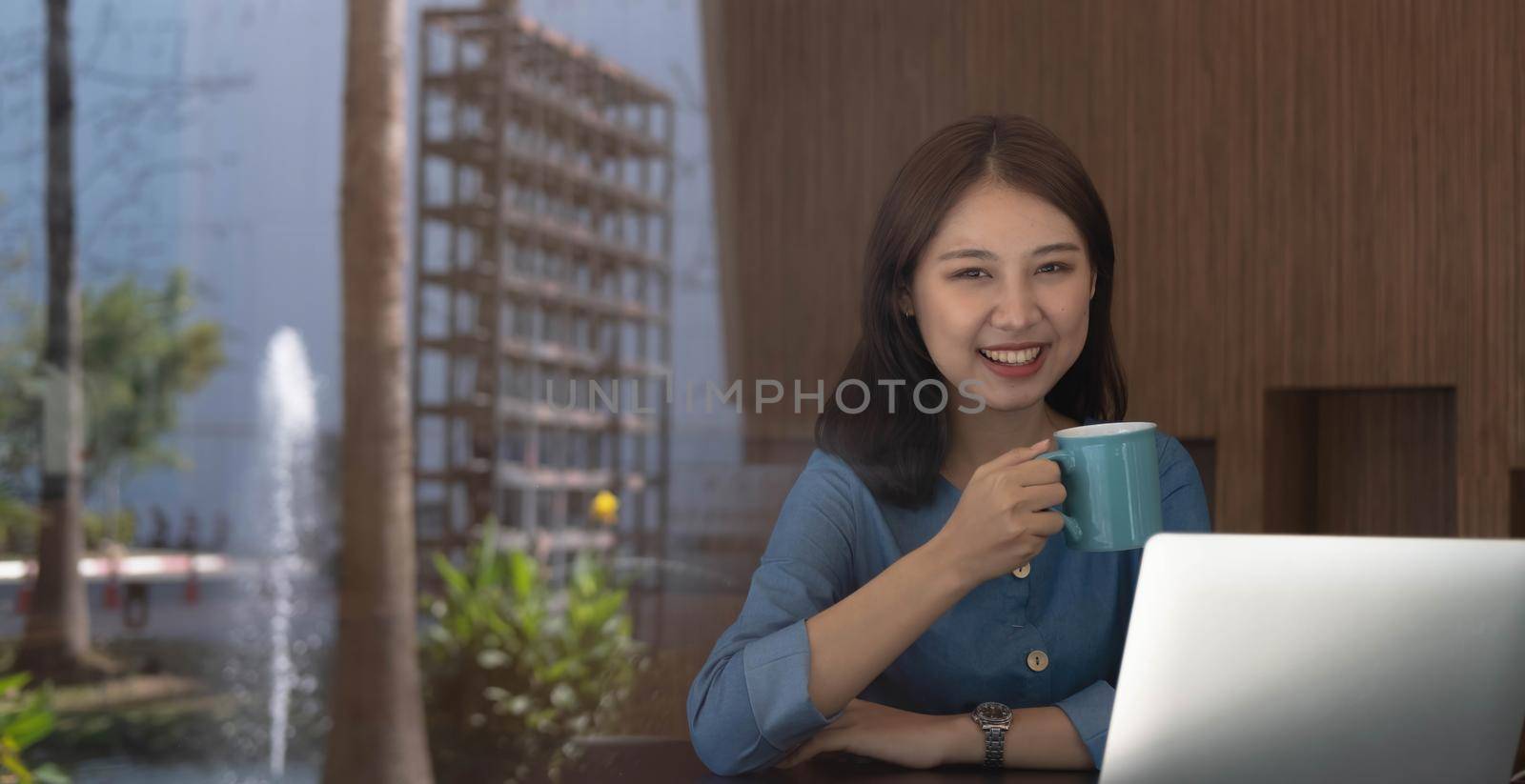 Smiling Asian businesswoman holding a coffee mug and laptop at the office. Looking at the camera..