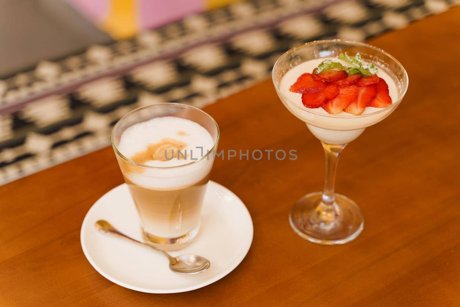 Creamy dessert with strawberries in glass, cappuccino on wooden table. Appetizing dessert and latte on the background of the restaurant.