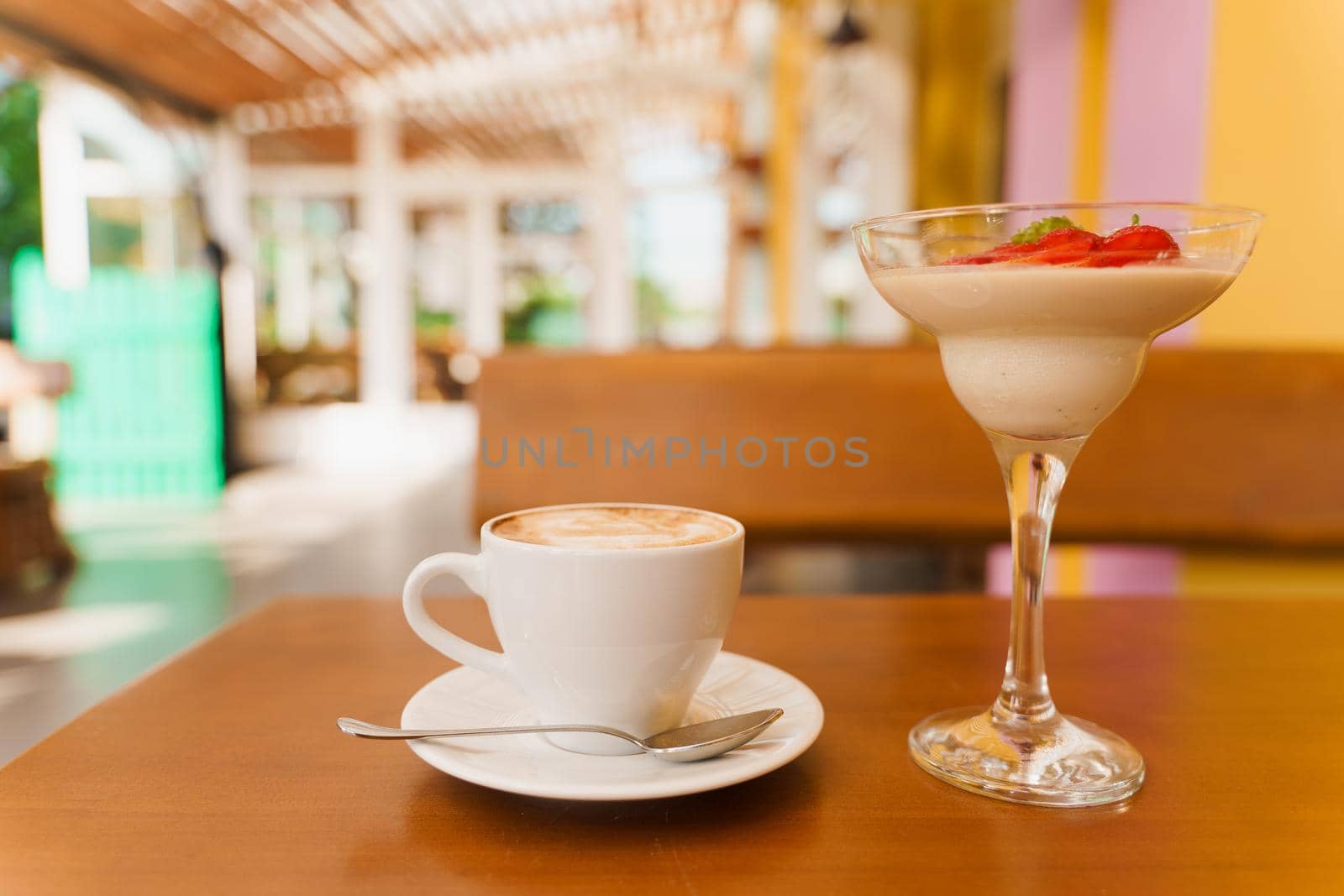 Creamy dessert with strawberries in glass, cappuccino on wooden table. Appetizing dessert and latte on the background of the restaurant.