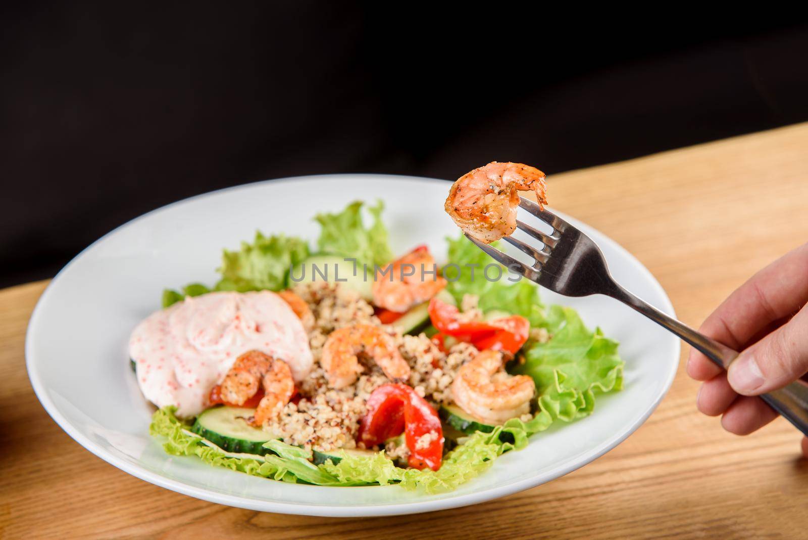 Salad with shrimps, quinoa, tomatoes, peppers, cucumber, lettuce, mayonnaise on white round plate on wooden table.