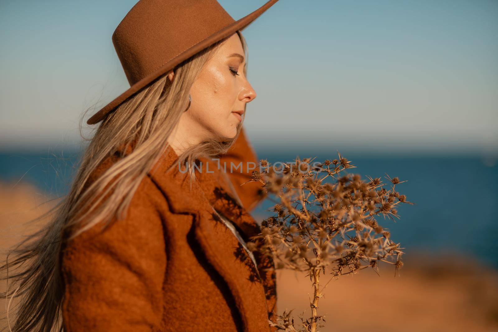 A woman walking along the coast near the sea. An elegant lady in a brown coat and a hat with fashionable makeup walks on the seashore by Matiunina
