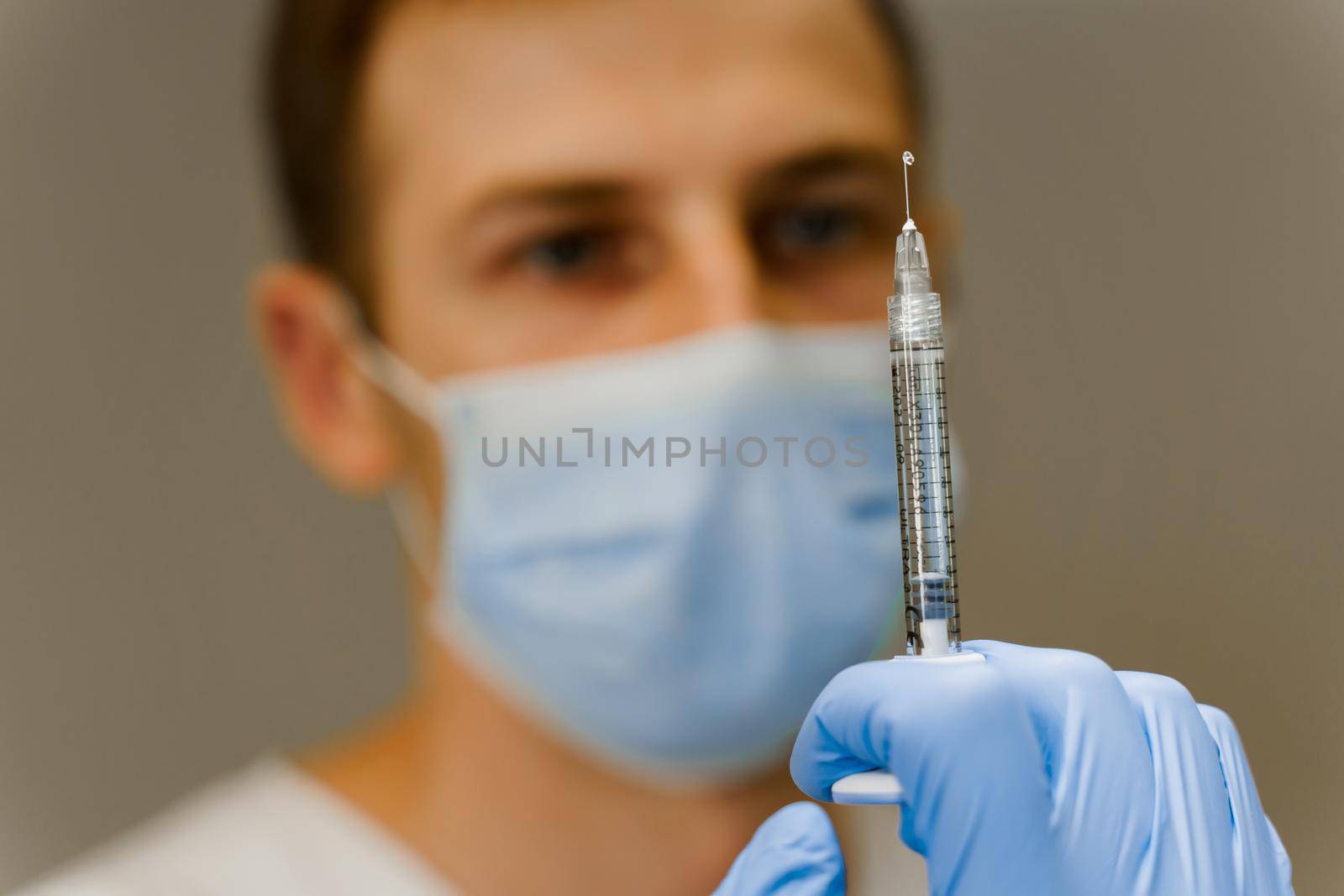 Doctor holds a syringe with a drop of medication at the end of the needle. Preparation before plastic surgery. Lips Augmentation