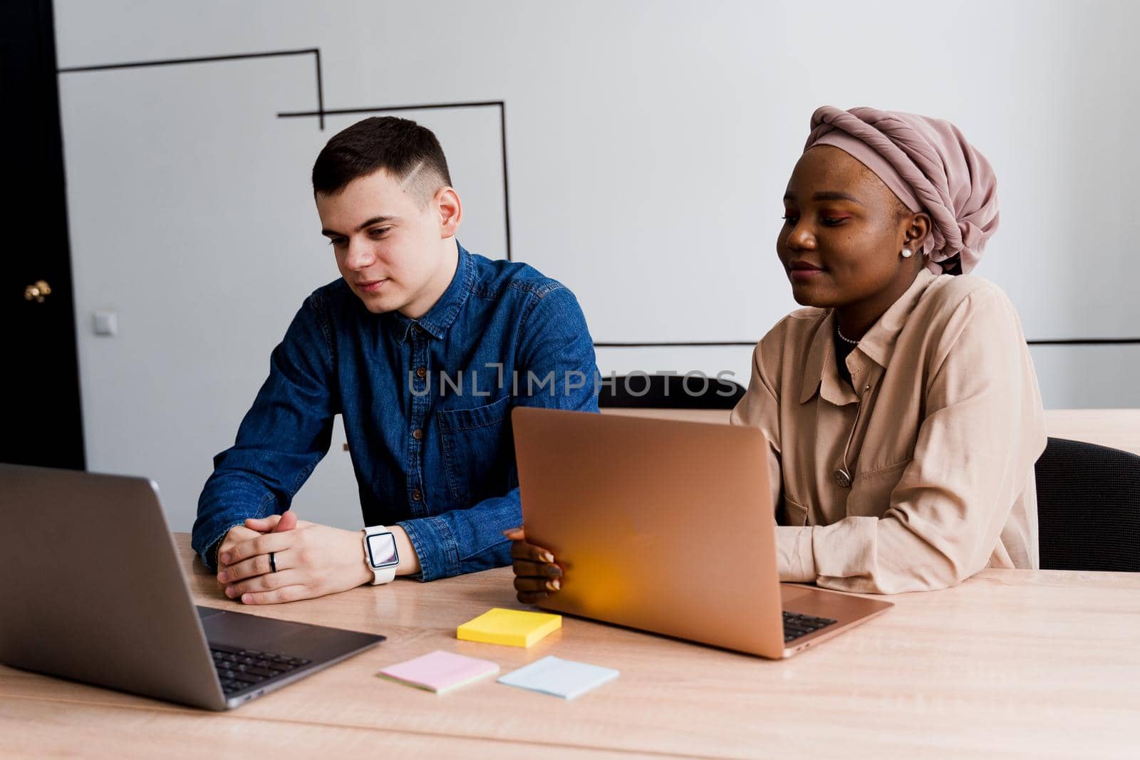 Muslim black girl and white man with laptop. Multiethnic couple work online together on business project. Working at home. Surfing internet.