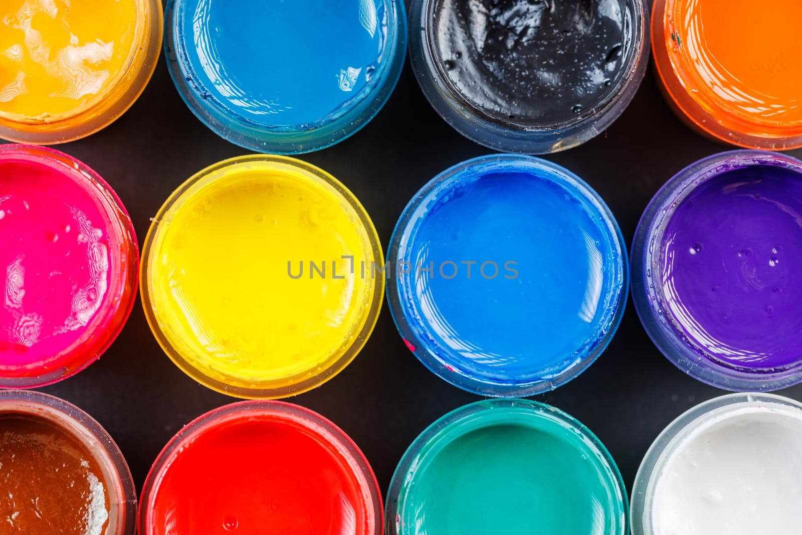 full-frame close-up background of opened small gouache paint jars on black