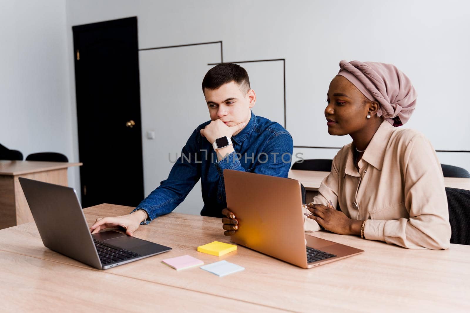 Muslim black girl and white man with laptop. Multiethnic couple work online together on business project. Working at home. Surfing internet by Rabizo