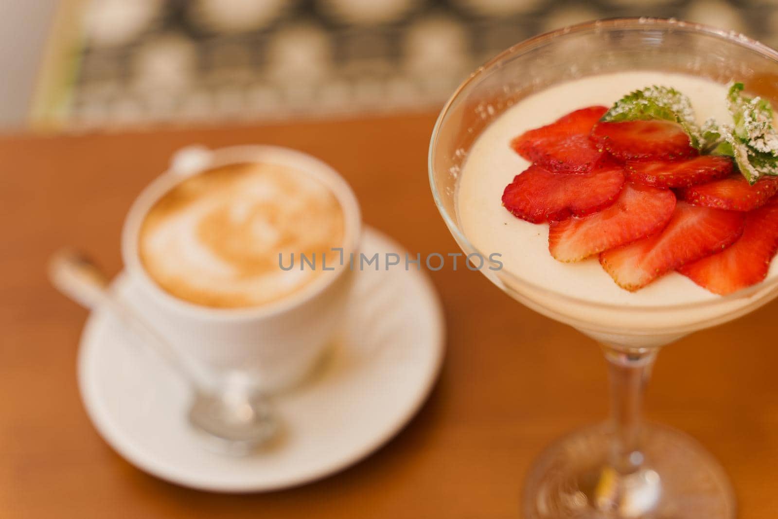 Creamy dessert with strawberries in glass, cappuccino on wooden table. Appetizing dessert and latte on the background of the restaurant.