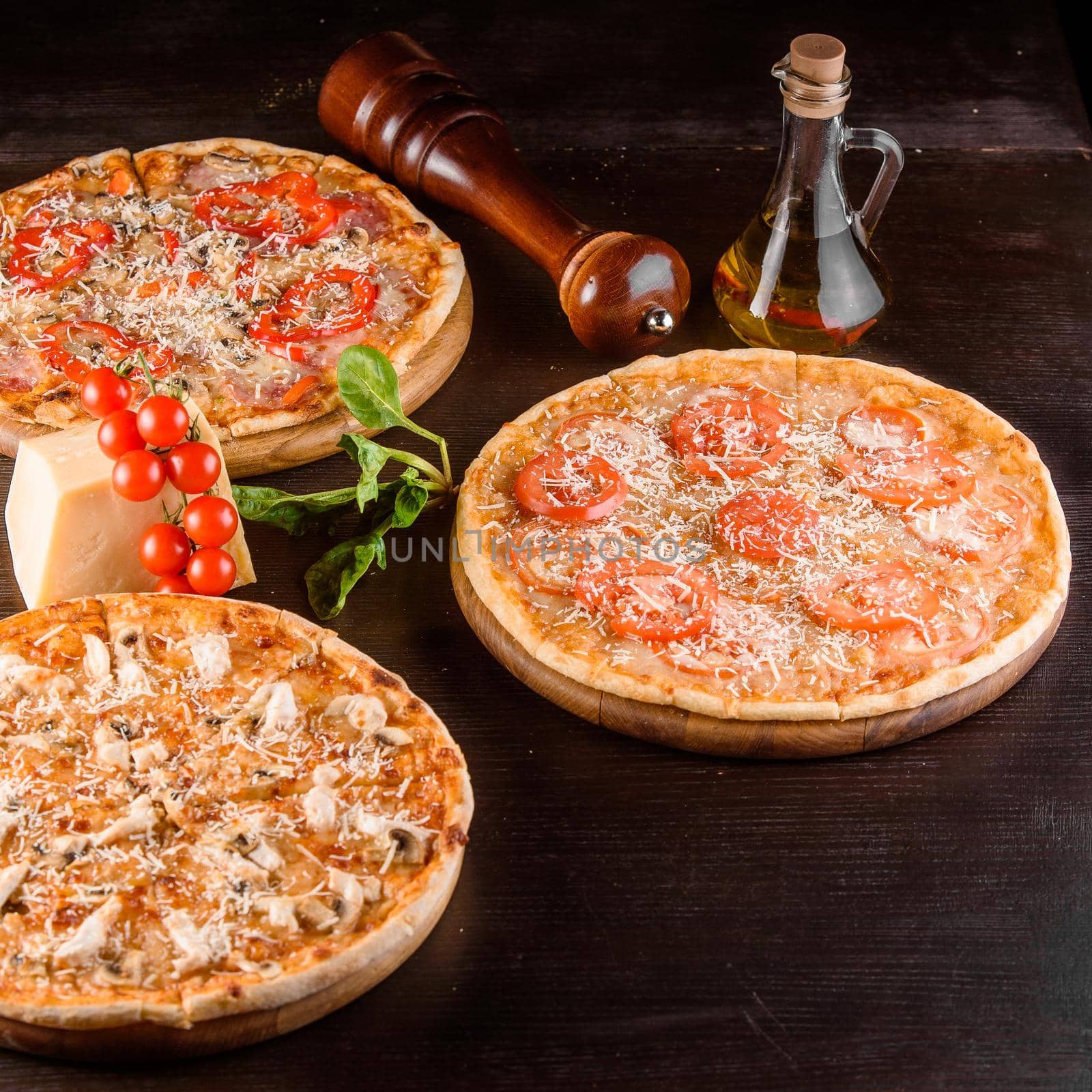 Pizza with chicken, mushrooms, cheese, sauce, ham, salami and pepper, tomatoes on a dark wooden table. Assortment of pizzas.