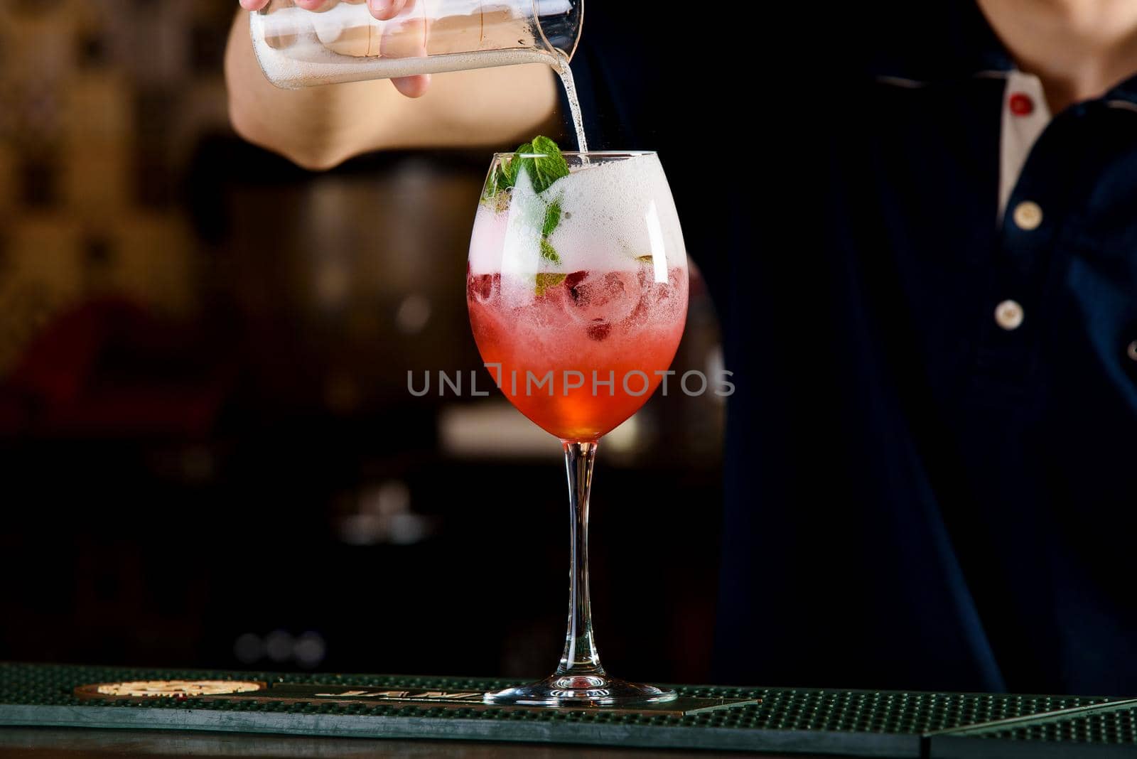 Orange alcoholic cocktail with berries and ice. Bartender preparing a cocktail.