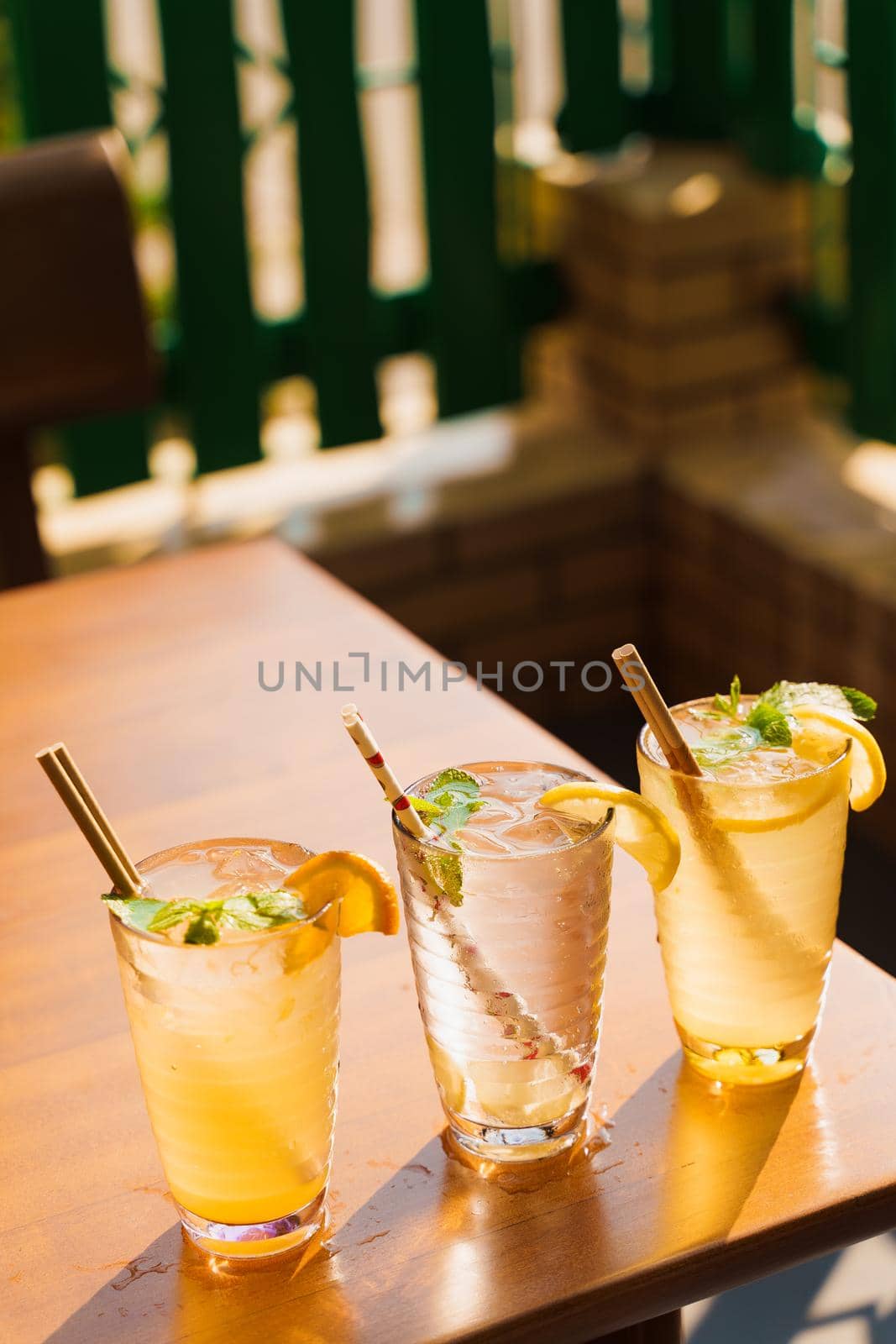 Cocktails with lemon and mint in glasses with tube on a wooden table against the background of a restaurant. Cold lemonade