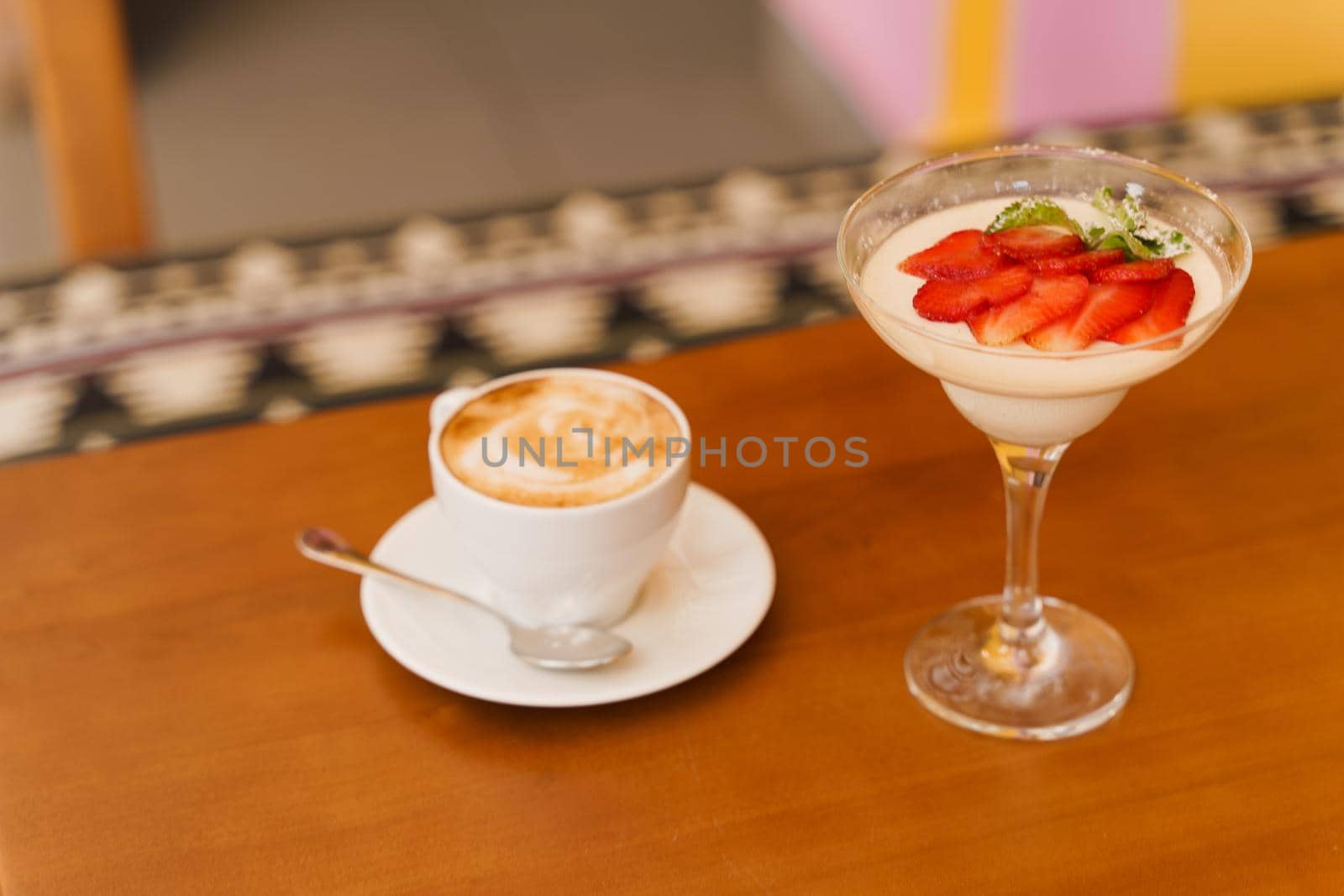 Creamy dessert with strawberries in glass, cappuccino on wooden table. Appetizing dessert and latte on the background of the restaurant.