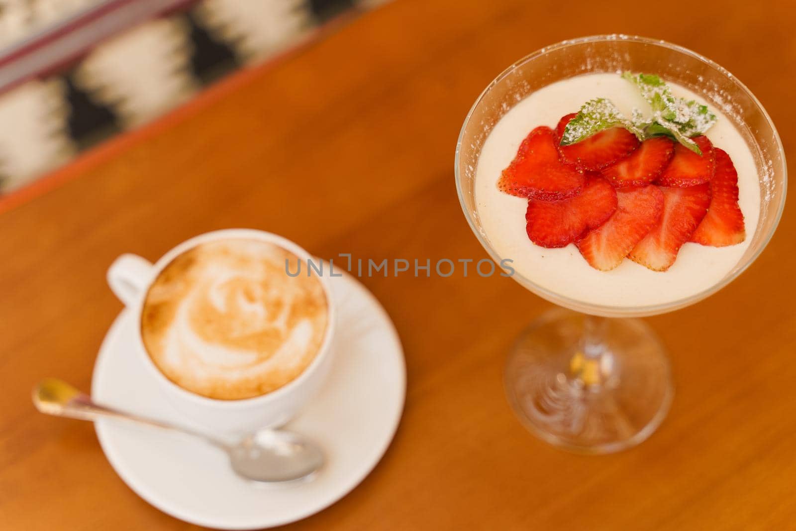 Creamy dessert with strawberries in glass, cappuccino on wooden table. Appetizing dessert and latte on the background of the restaurant.