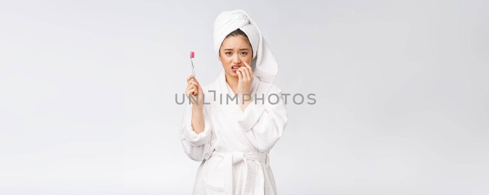 Unhappy beautiful woman brushing her teeth on white background.