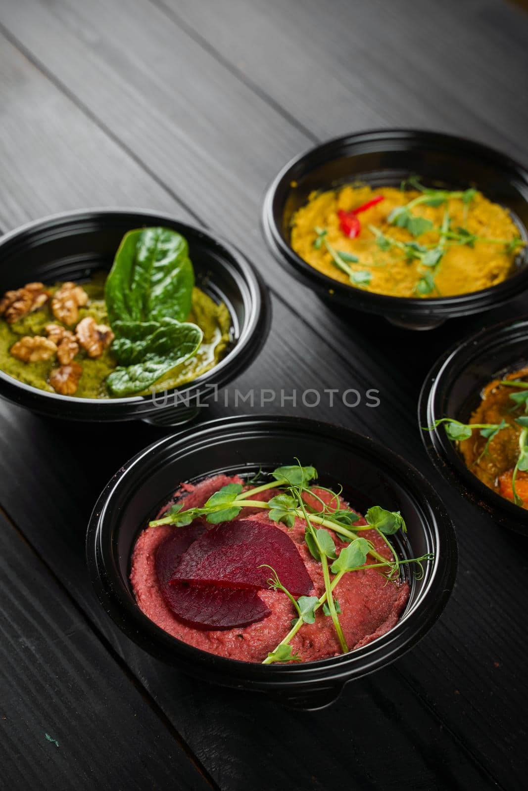 Hummus garnished peppers, chili, beet and herbs in black bowl on dark wooden table. Hummus assortment.