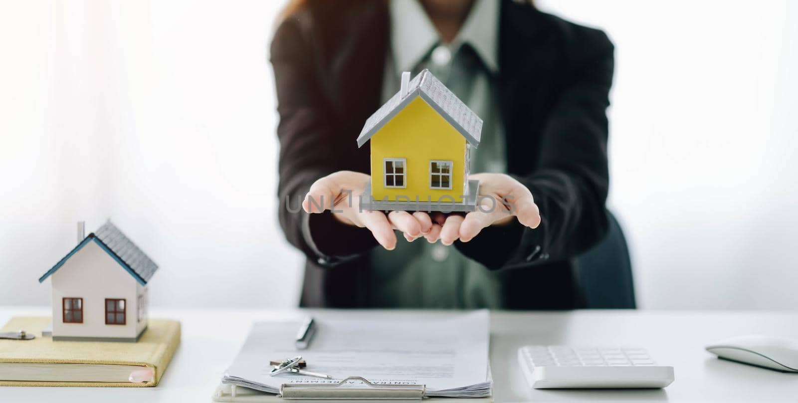 Miniature house in the hands of an Asian woman real estate agent home loan working at the office. Looking at the camera..