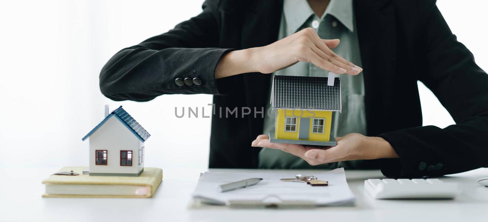 Miniature house in the hands of an Asian woman real estate agent home loan working at the office.