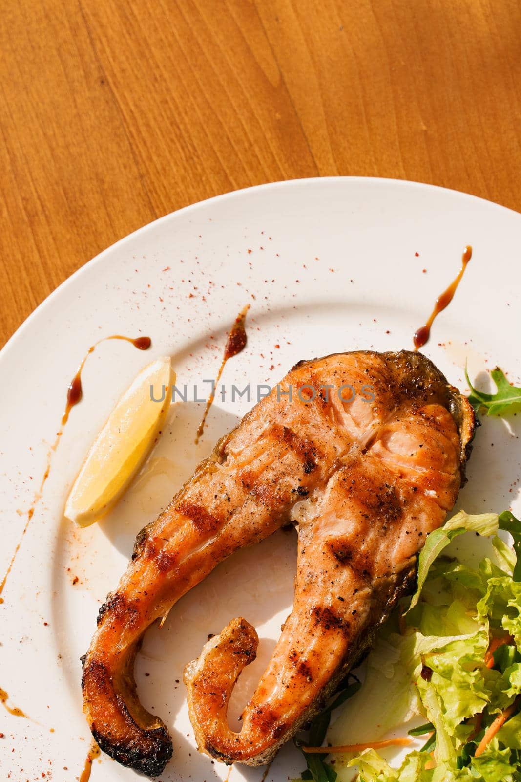 Grilled salmon steak with lettuce and lemon on a white plate on a wooden table