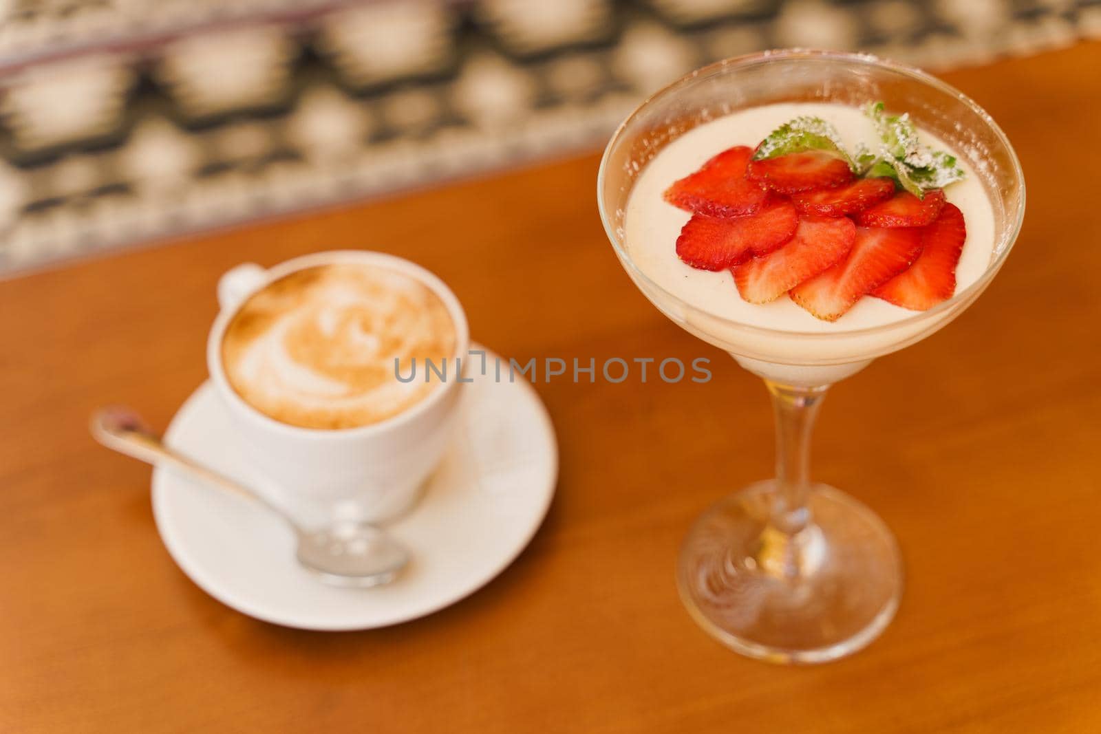 Creamy dessert with strawberries in glass, cappuccino on wooden table. Appetizing dessert and latte on the background of the restaurant by Rabizo