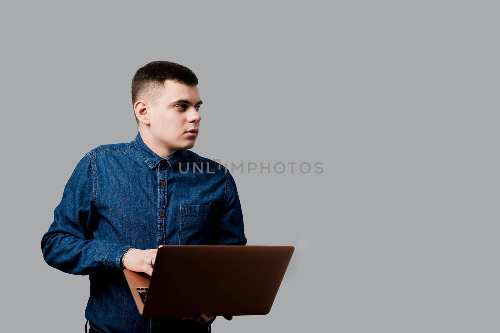 Handsome man with laptop on the gray background. Business man working online at home by Rabizo