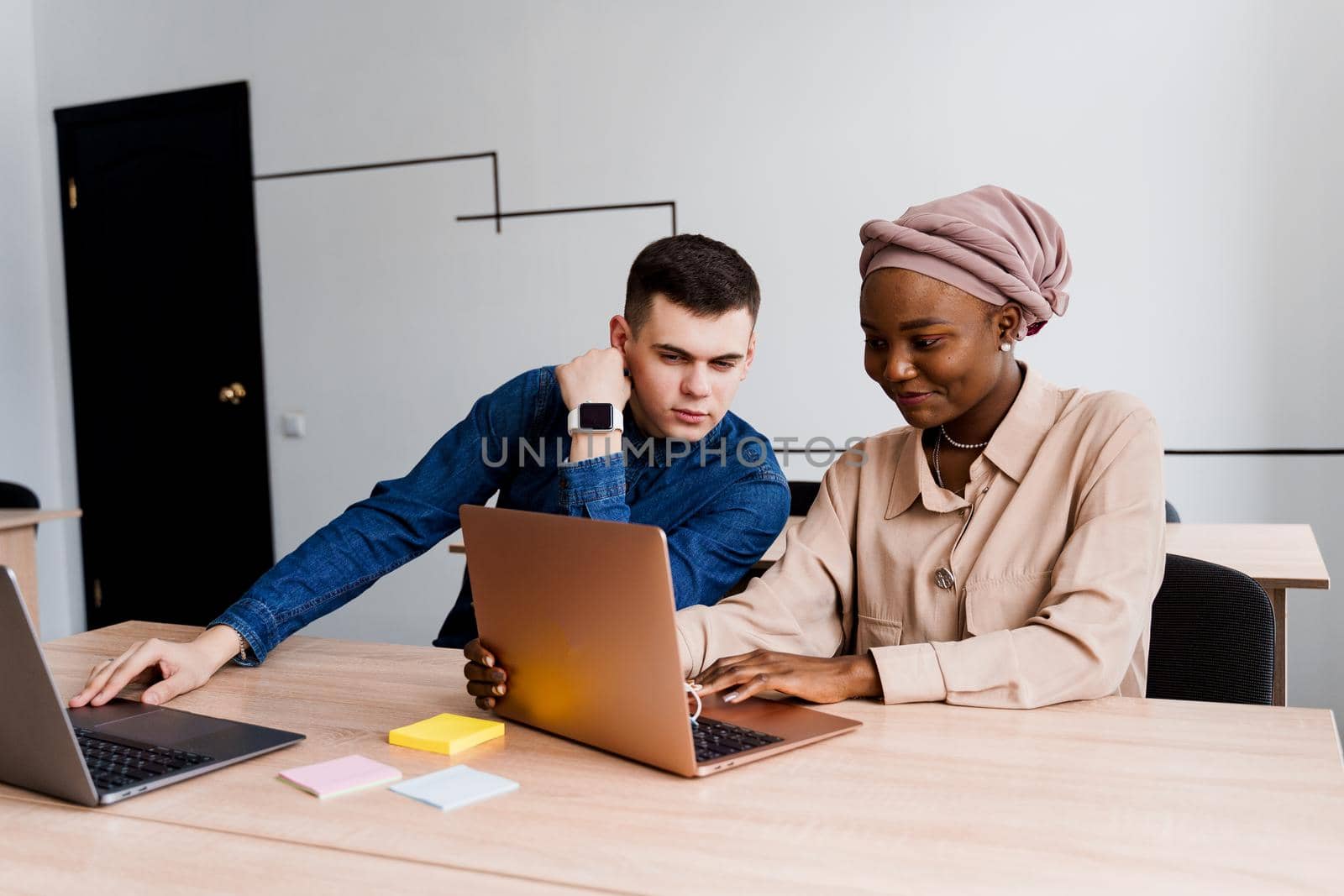 Muslim black girl and white man with laptop. Multiethnic couple work online together on business project. Working at home. Surfing internet.