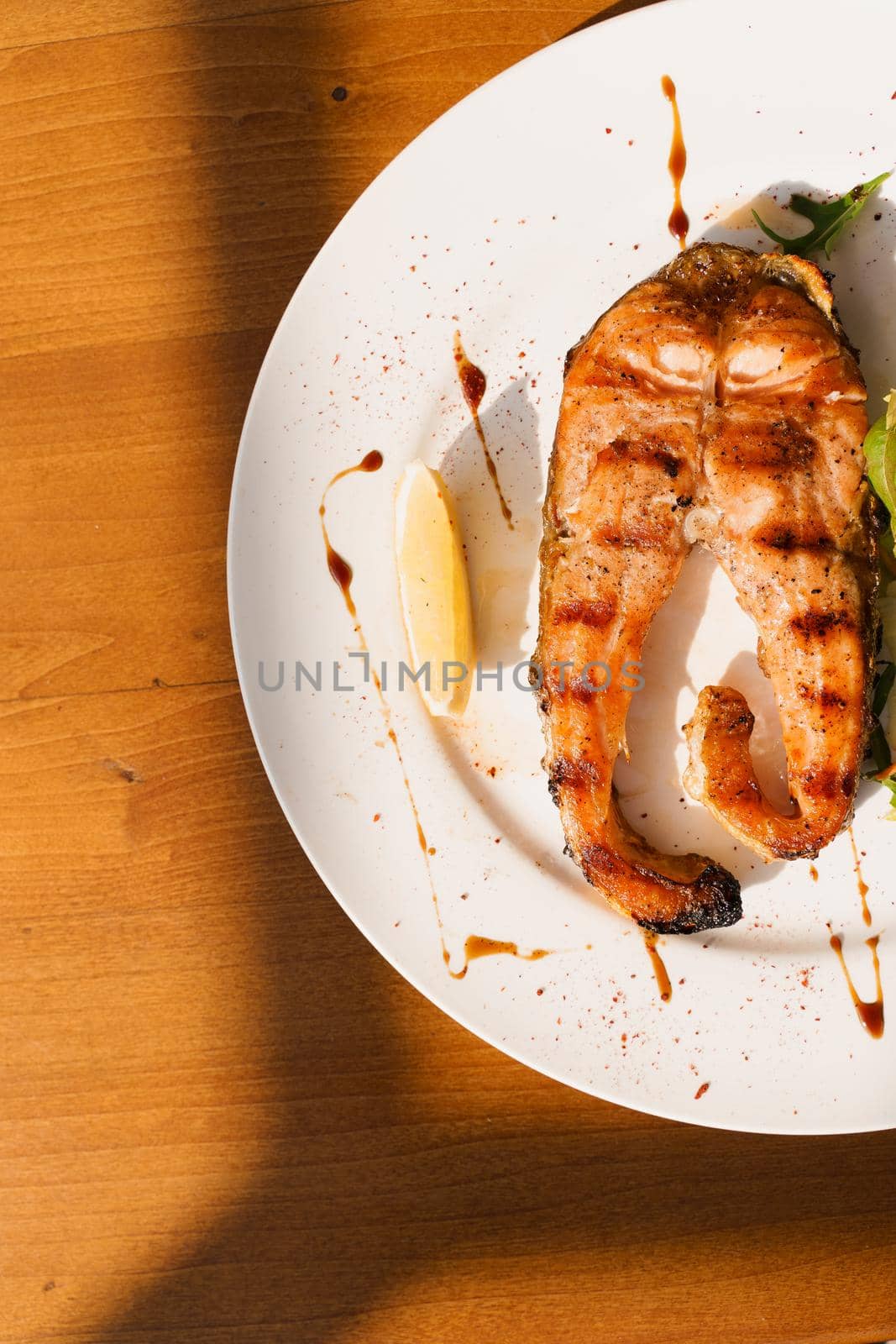 Grilled salmon steak with lettuce and lemon on a white plate on a wooden table