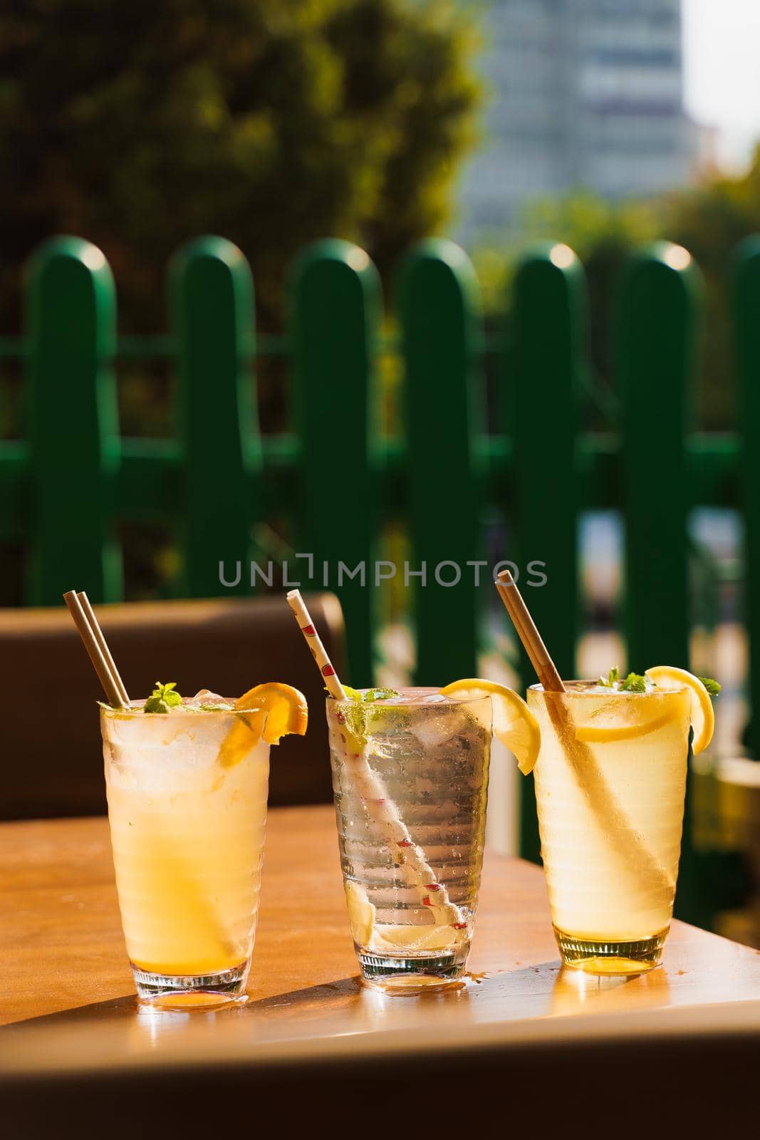 Cocktails with lemon and mint in glasses with tube on a wooden table against the background of a restaurant. Cold lemonade