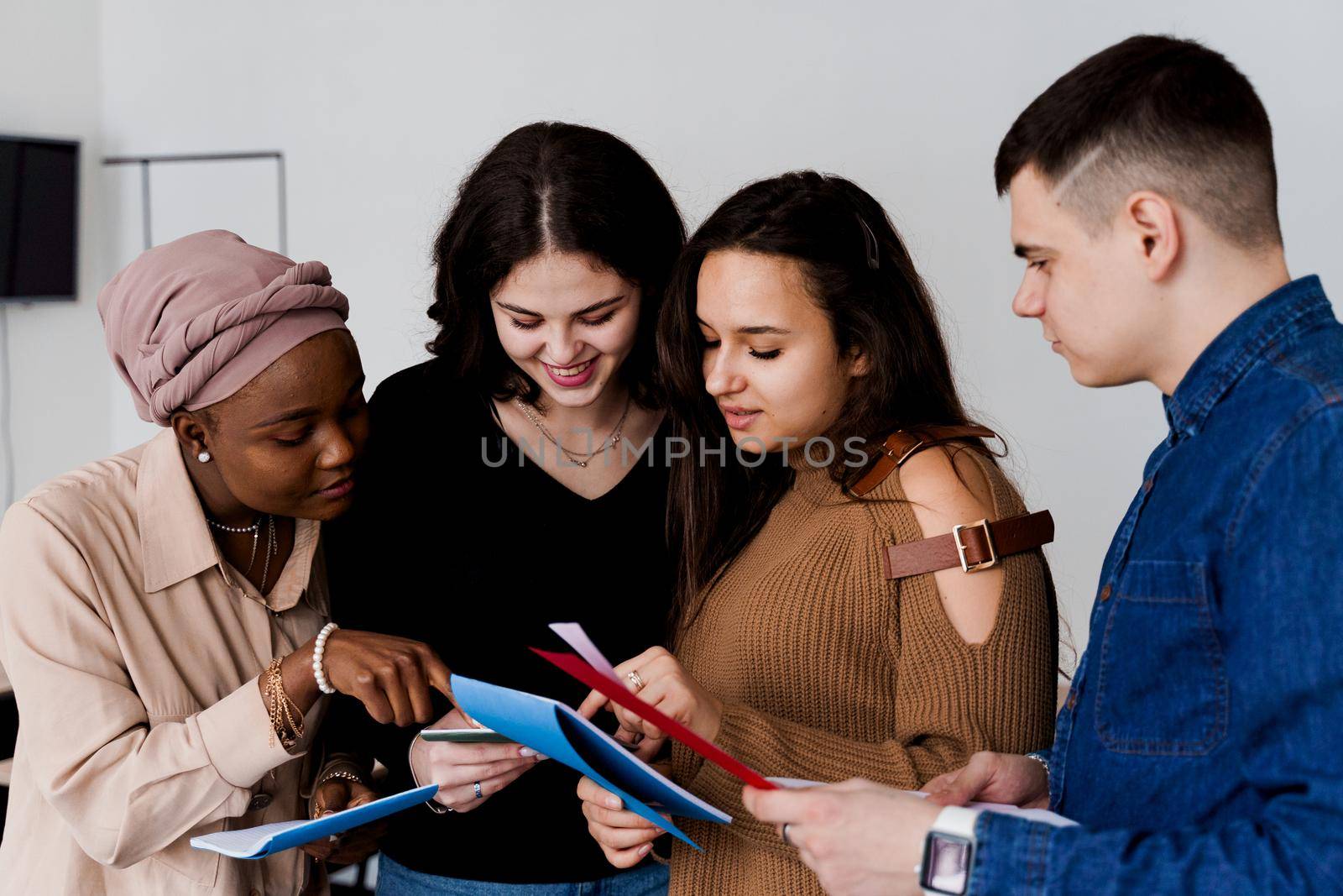 Multiethnic students and teacher study foreign languages together in class. Studing with notebook. Black attractive girl student study with white people together and look into camera. by Rabizo