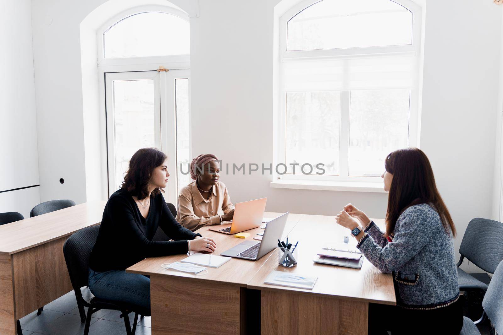 Multiethnic students and teacher study foreign languages together in class. Studing with laptop. Black handsome girl student study with white people together and look into camera. by Rabizo