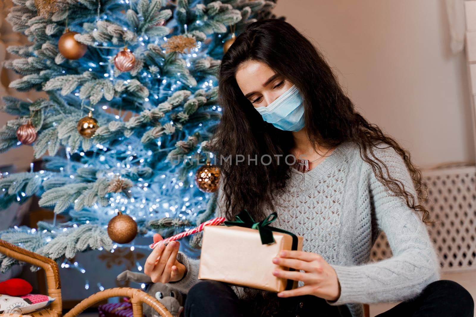 Girl in a medical mask with a Christmas present and candy. celebration of the new year on self-isolation. Pandemic coronavirus covid-19 concept. Advertising sale during the quarantine period